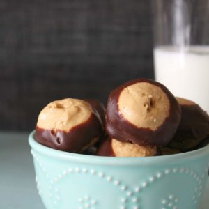 homemade buckeyes in a light blue bowl with a glass of milk in the background