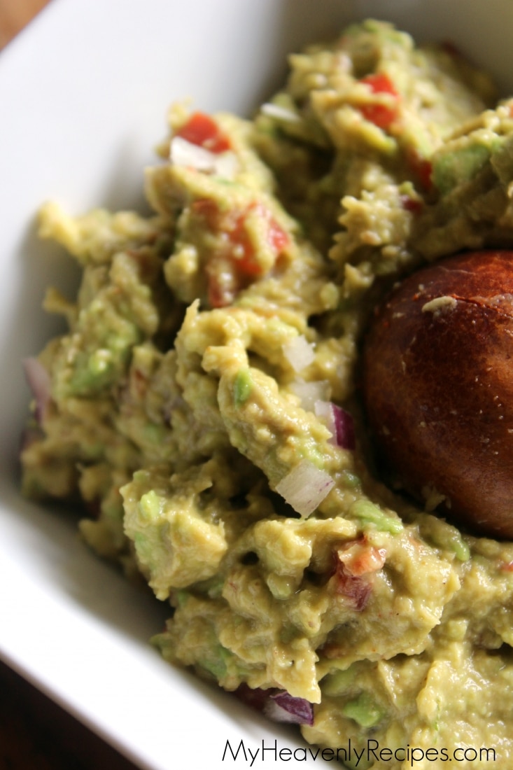 Tight shot of homemade guacamole with avocado pit in a white bowl