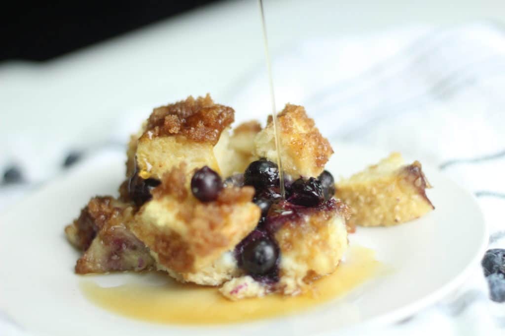 drizzling maple syrup over blueberry french toast bake on white plate