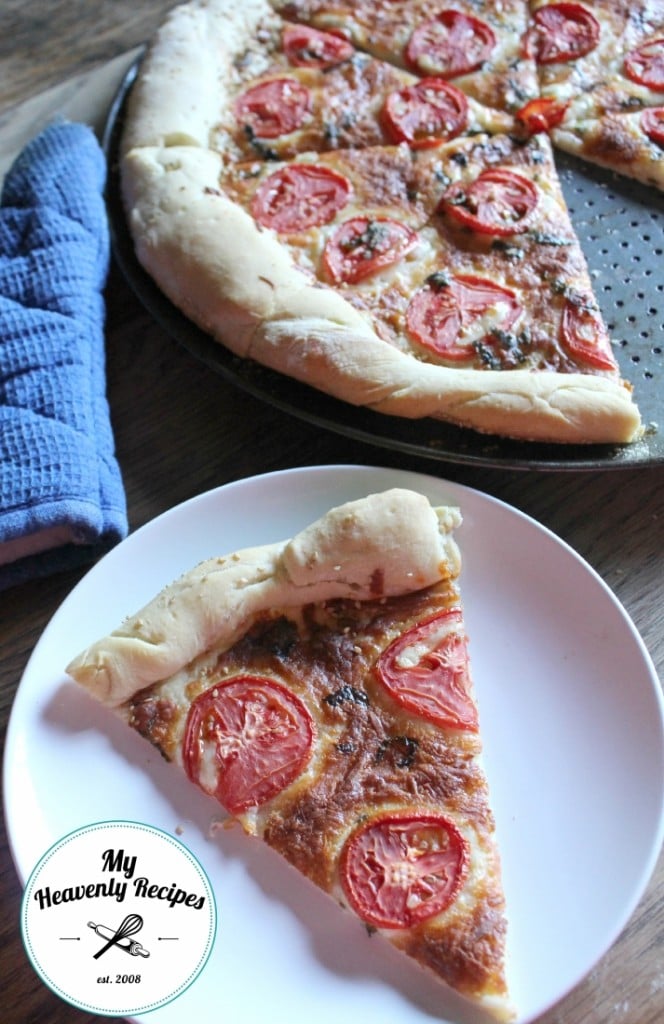 margherita pizza with tomato and cheese on a homemade pizza crust served on a white plate with cooked pizza on pizza pan in background and oven mit on table