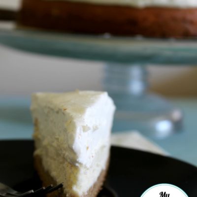 vanilla bean cheesecake on black plate with cake stand in the background with the full cheesecake