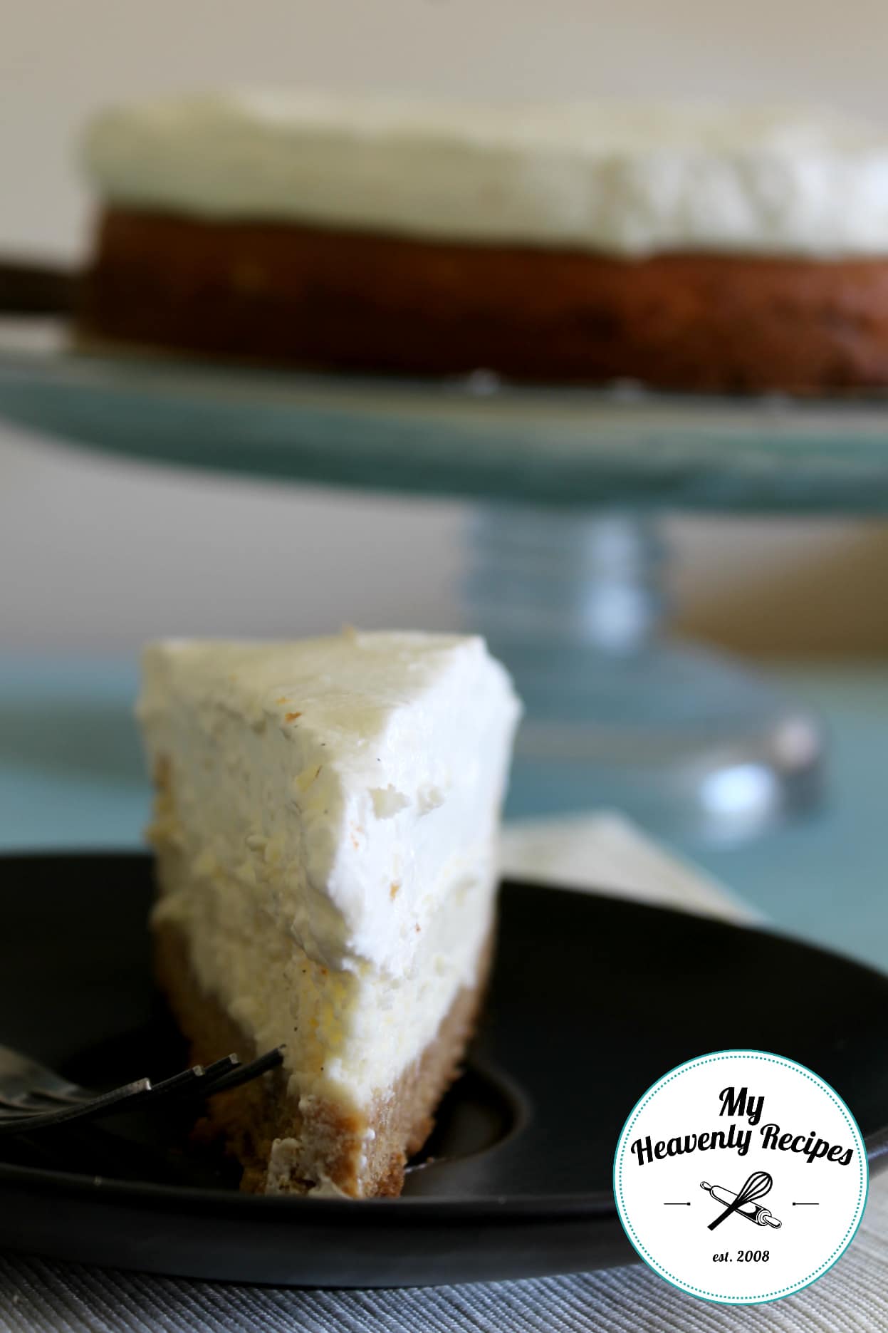 vanilla bean cheesecake on black plate with cake stand in the background with the full cheesecake