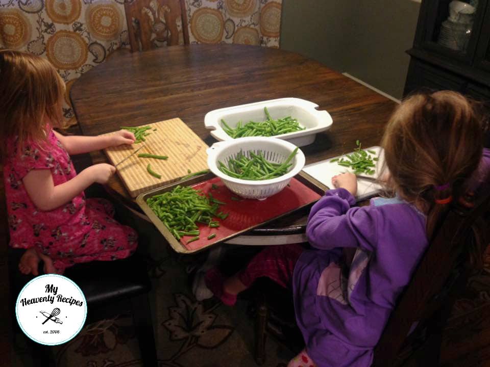 2 little girls sitting at a table trimming green beans on cutting boards