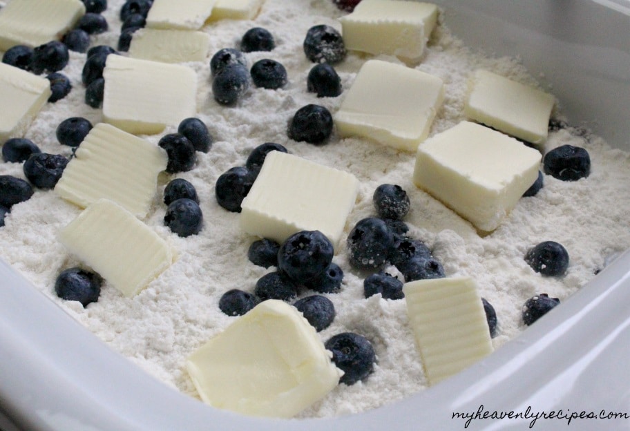 ingredients needed to make crock pot dump cakes - shown: white cake mix, fresh blueberries, and squares of cold butter