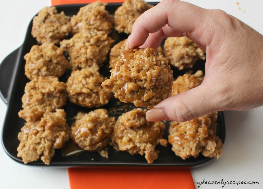 muffin tin holding a batch of the best pumpkin muffins with streusel. A hand is holding a muffin above the pan