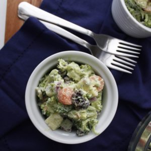 Broccoli Avocado Salad in white bowl with forks on table and blue napkin