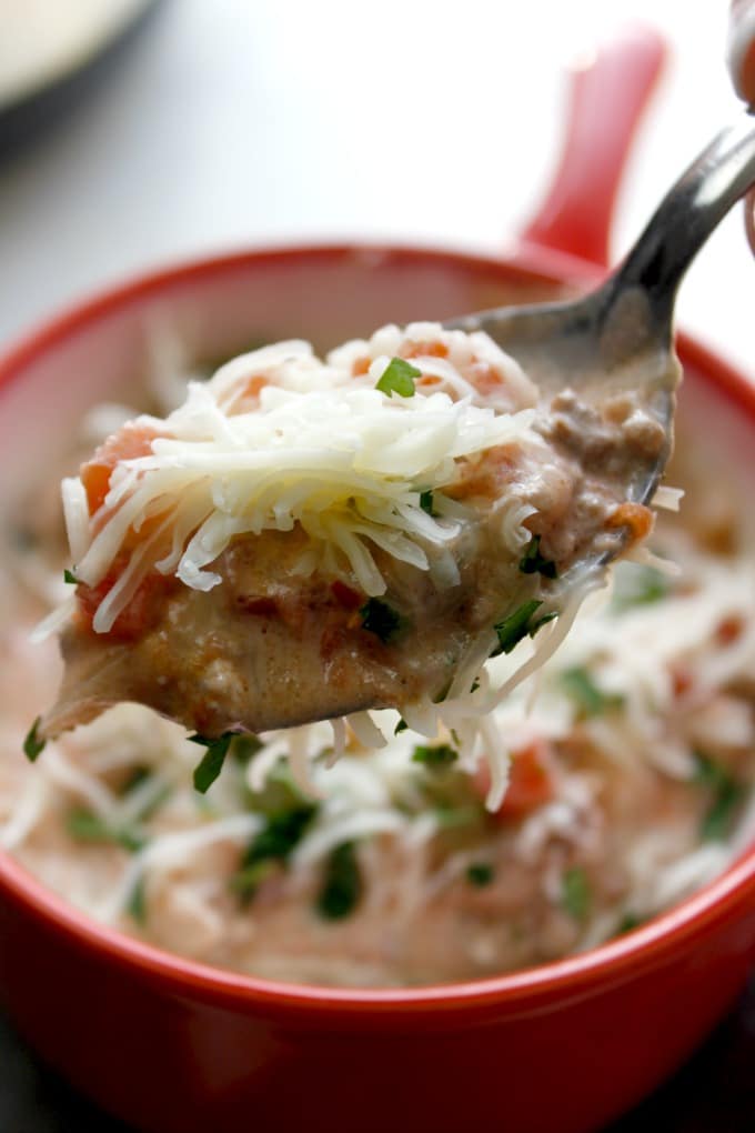 closeup of low carb taco soup on a spoon being held over bowl of low carb taco soup