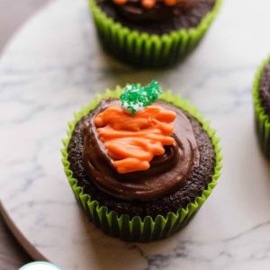 two Easter chocolate cupcakes with chocolate icing topped with candy carrots