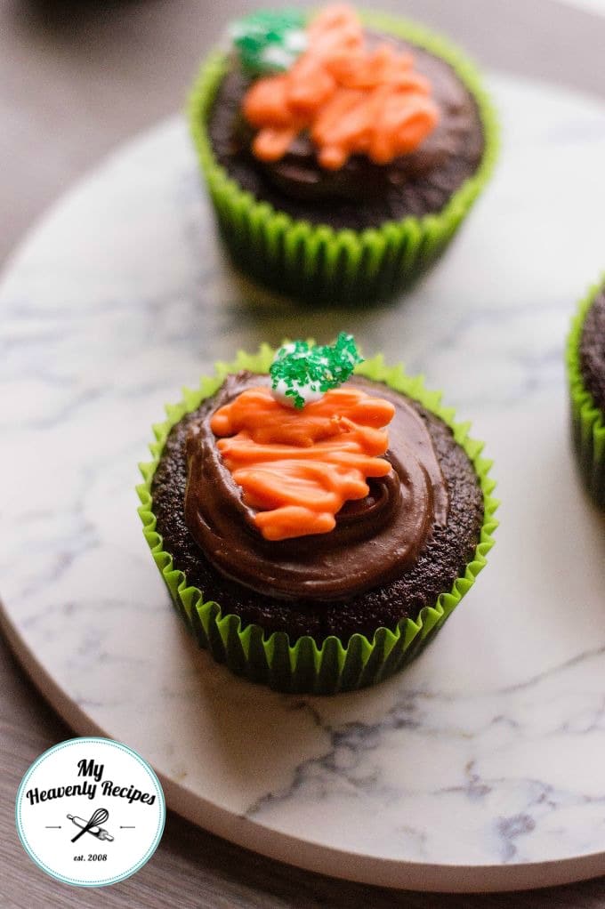 two chocolate easter cupcakes on a platter with chocolate icing topped with candy carrot