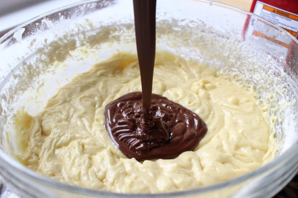 pouring melted chocolate into bowl with ingredients for brownie recipe