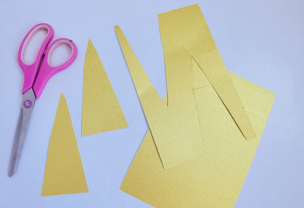 yellow paper cut up next to pink scissors for unicorn craft plate