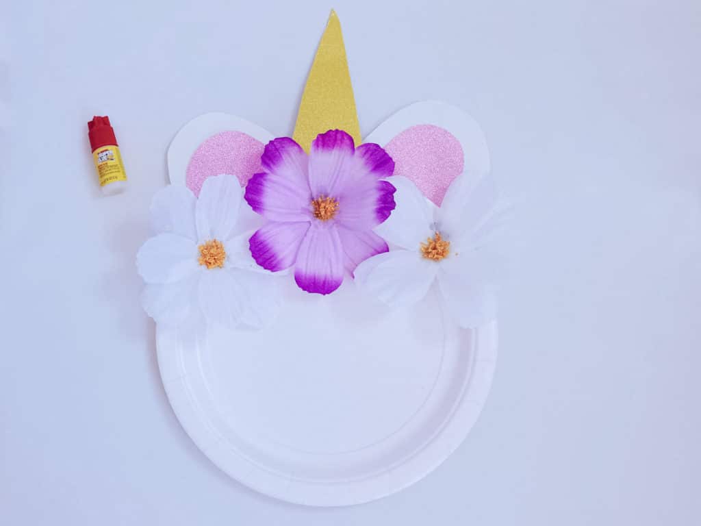 unicorn craft plate almost fully complete with flowers on top next to glue