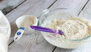 mixing in flour in glass bowl with measuring cup on table
