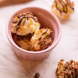 chocolate drizzled coconut macaroons in a bowl with a few on a marble surface