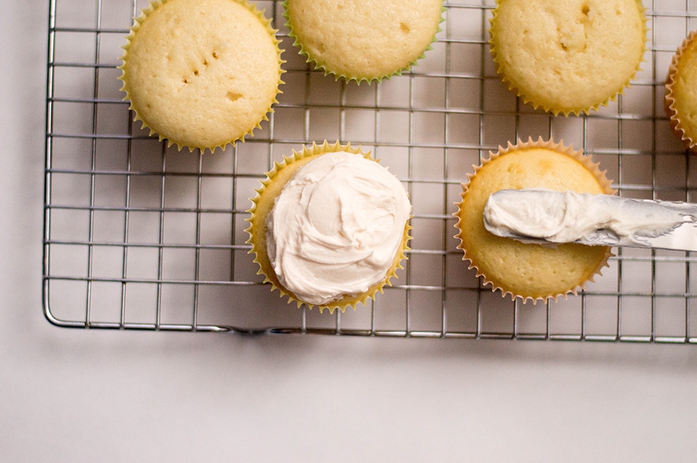 moist vanilla cupcakes being frosted on a wire rack