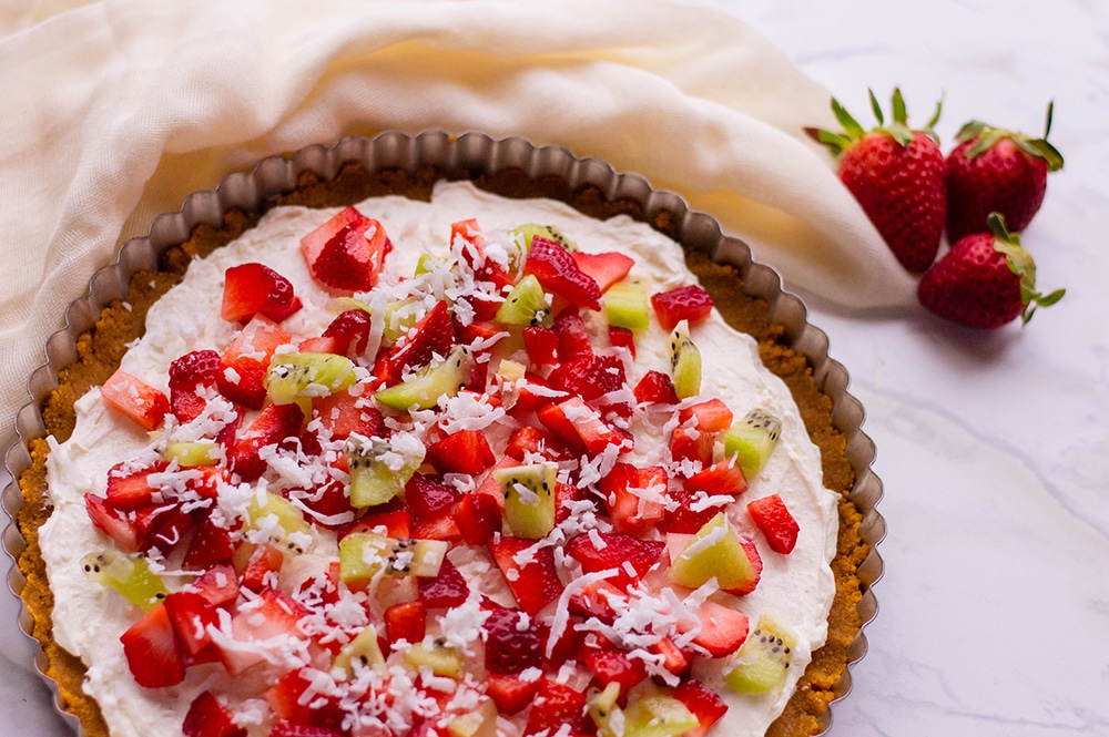 image of dessert pizza recipe with strawberries and kiwi topped with coconut flakes with linen napkin in background vertical image
