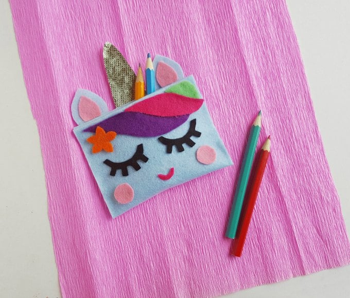 unicorn pencil case next to two pencils and on top of pink felt