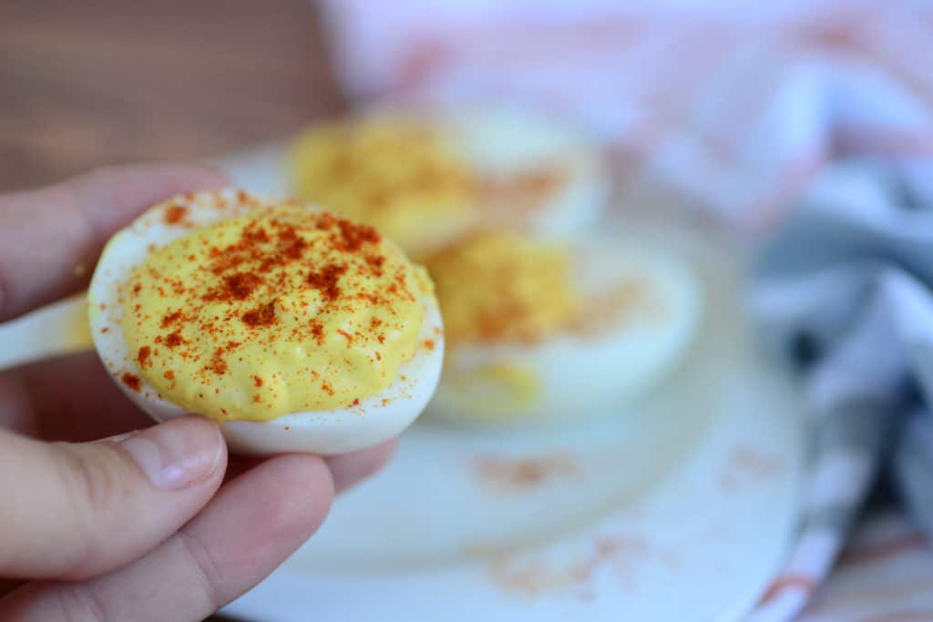 close up shot of hand holding deviled egg sprinkled with paprika