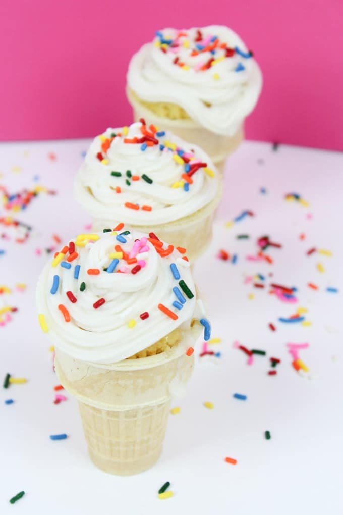 three ice cream cone cupcakes lined up with sprinkles around them