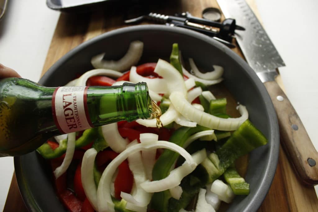 pouring yuengling beer into metal dish with peppers and onions