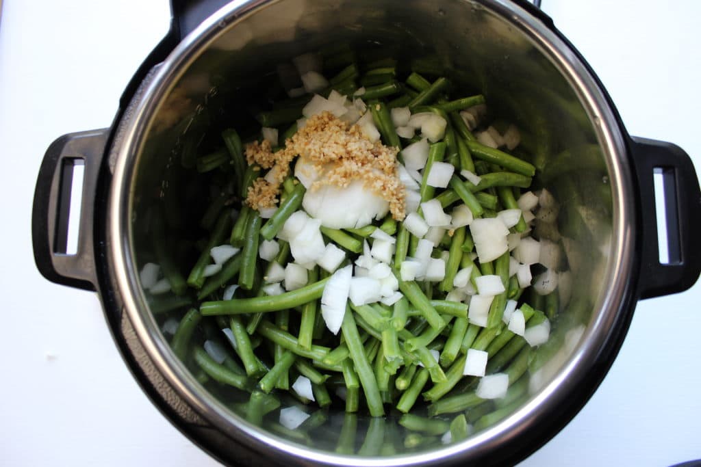 overhead shot of green beans, onions and garlic in instant pot