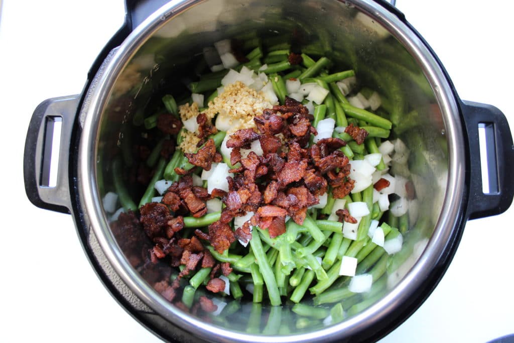 overhead shot of green beans, onions, garlic and bacon in instant pot