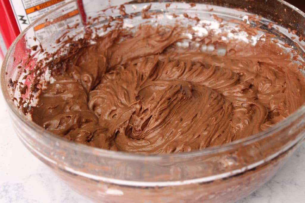 chocolate fudge icing in glass bowl with hand mixer