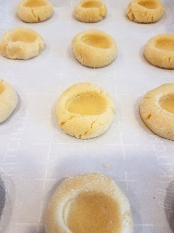 thumbprint cookies on baking sheet with parchment paper with indentation in dough
