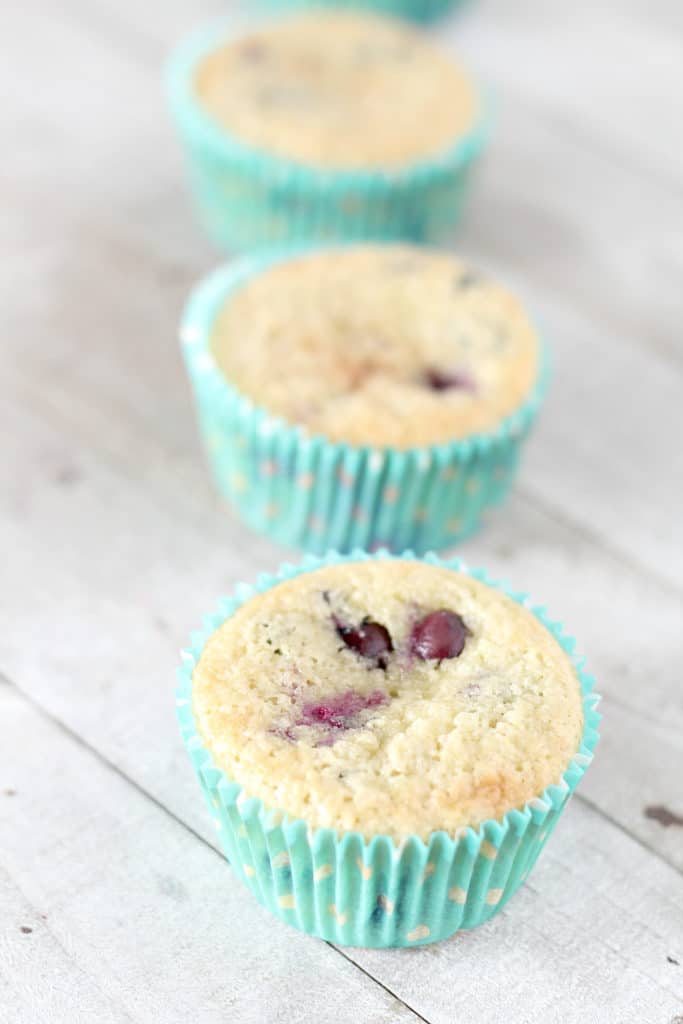 3 keto blueberry muffins in teal liners on wood grain background
